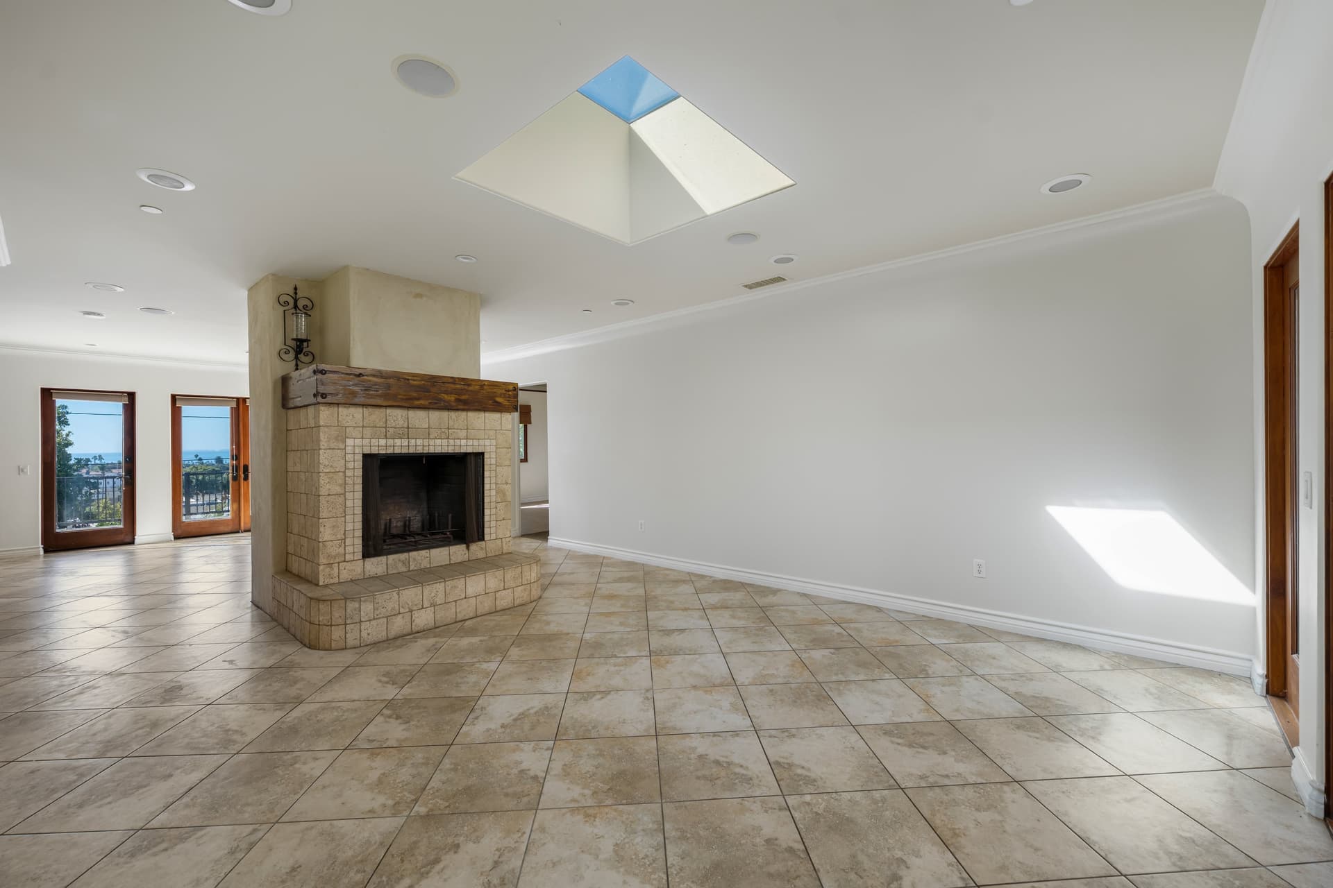 Empty living room with a tiled fireplace, recessed lights off and a bright sun patch on the wall