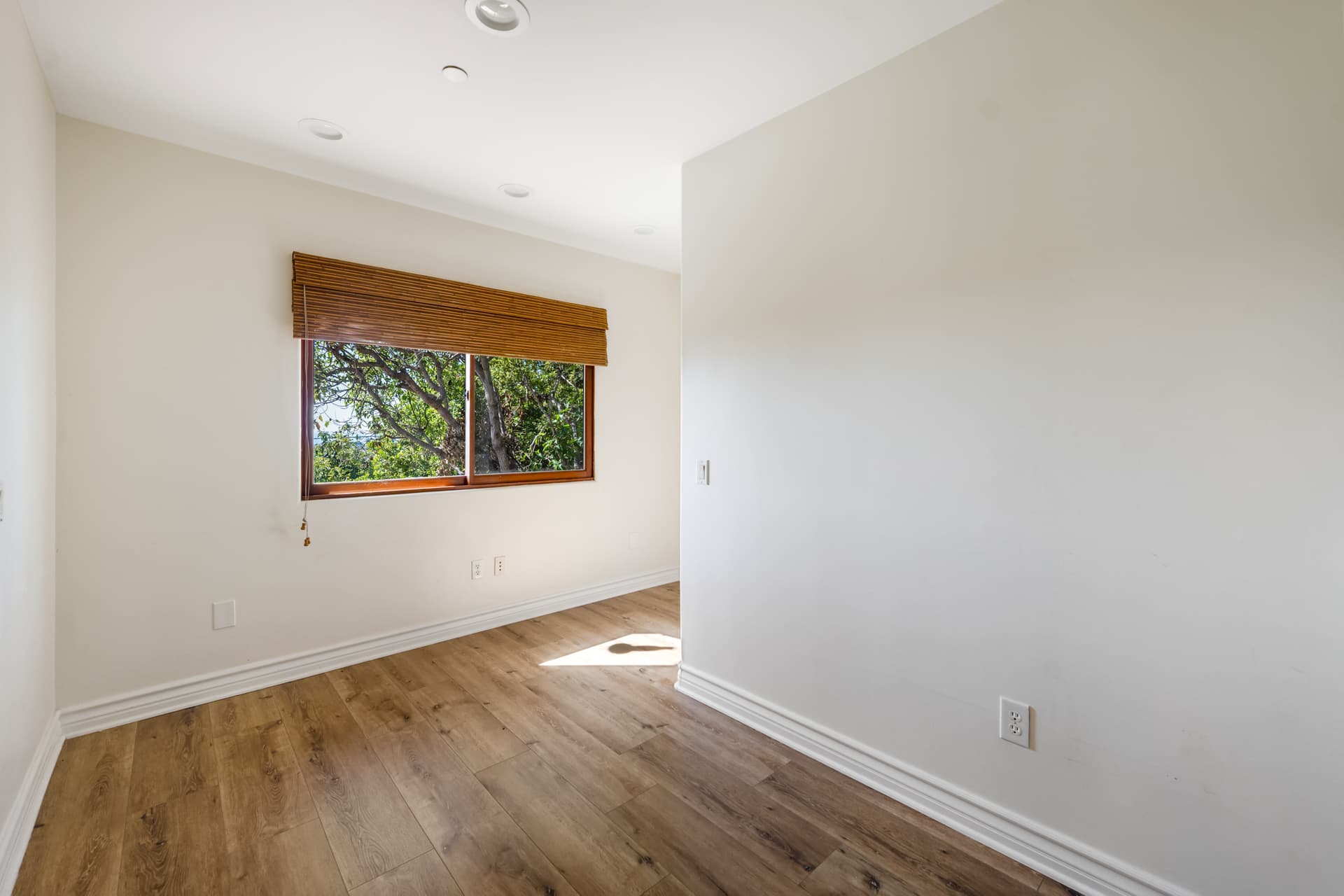 Empty bedroom in daylight with recessed lights off and a bright sun patch on the wood floor