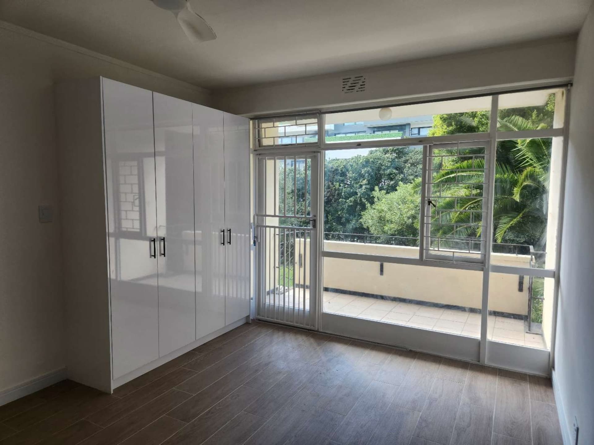 Empty bedroom with a white wardrobe and balcony doors, photographed dim and slightly grey